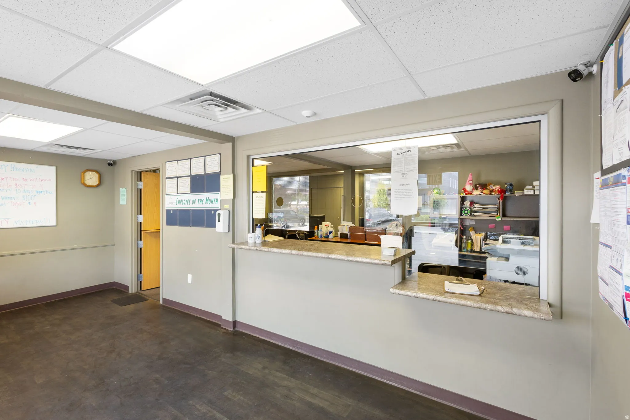 Welcoming reception area featuring a spacious front desk with granite countertop, abundant overhead lighting with recessed fixtures, neutral wall finishes, and dark tile flooring