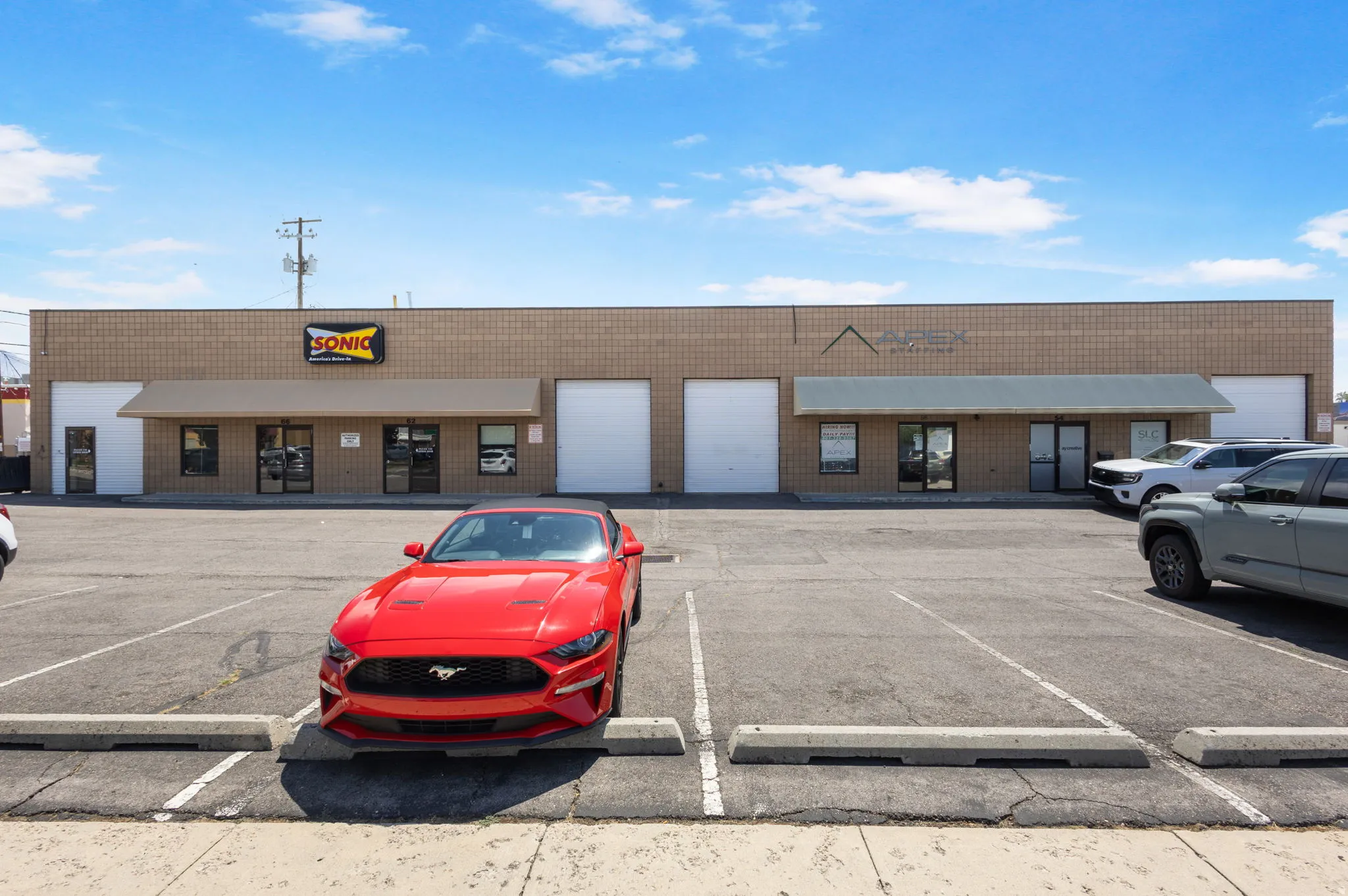 Commercial retail space featuring a multi-bay storefront with large display windows, roll-up garage doors, and ample front parking