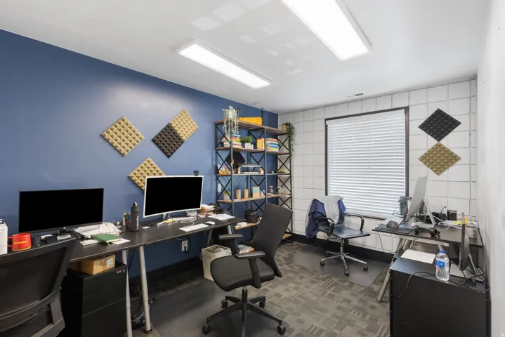 Modern office space featuring a dual-workstation layout with sleek black desks, ergonomic task seating, and integrated storage shelving