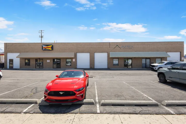 Commercial retail space featuring a multi-bay storefront with large display windows, roll-up garage doors, and ample front parking