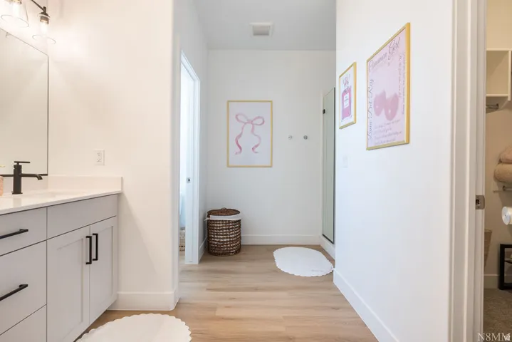 Primary Bathroom Suite featuring dual vanity with white cabinetry, black hardware accents, and wood-finish flooring throughout