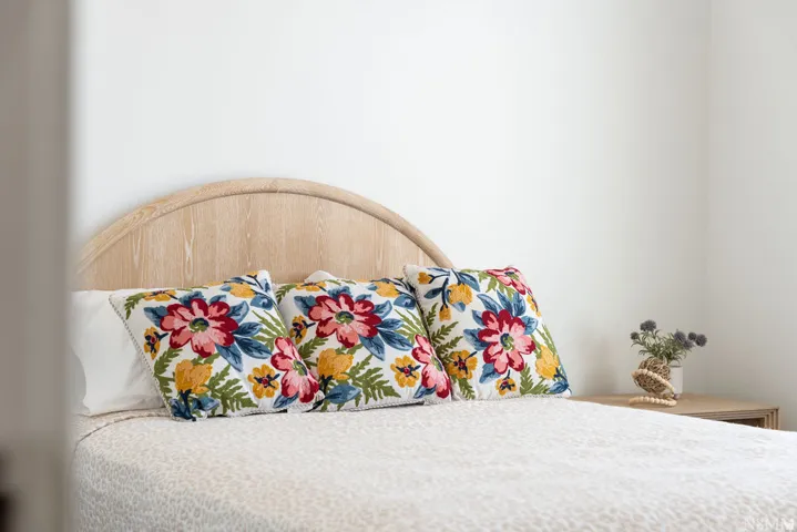 Serene primary bedroom showcasing a curved wood-finish headboard, crisp white bedding, and vibrant floral accent pillows