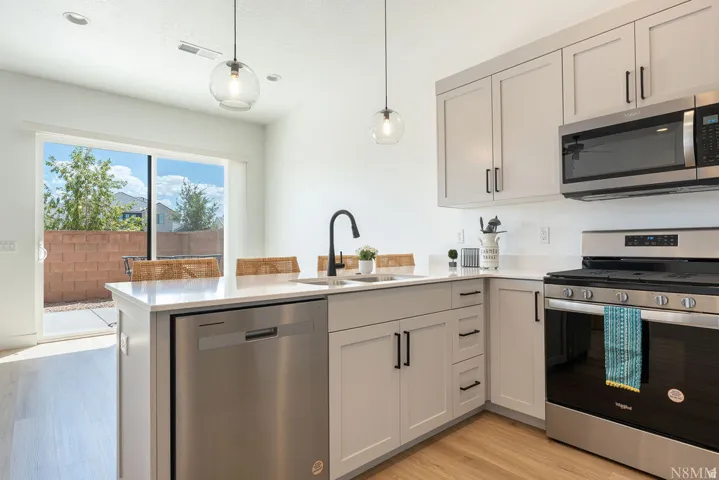 Modern kitchen featuring light cabinetry, stainless steel appliances, a white countertop, and wood-finish flooring