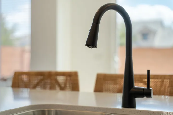 Modern matte black gooseneck faucet with an integrated pull-down spray head, set against a light countertop with a stainless steel sink