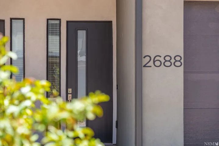 Modern entry featuring a sleek black pivot door with integrated sidelights, complemented by clean-lined architectural detailing and contemporary house numbering