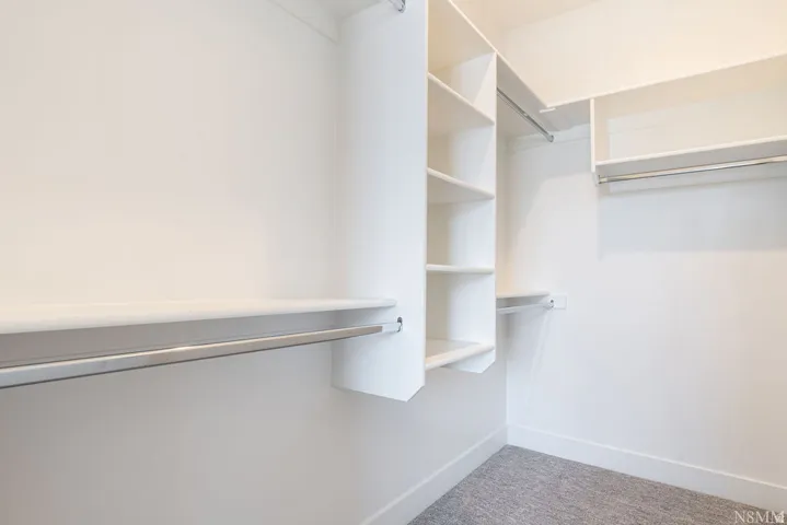 Spacious walk-in closet featuring multiple built-in shelving units, chrome hanging rods, and neutral finishes throughout