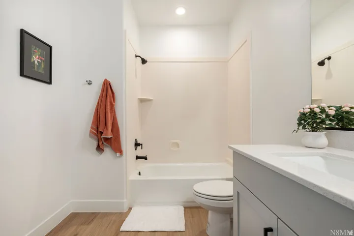 Contemporary bathroom featuring a tub/shower combination with matte black fixtures, a white vanity with an integrated sink and light-colored countertop, recessed lighting, and wood-finish flooring