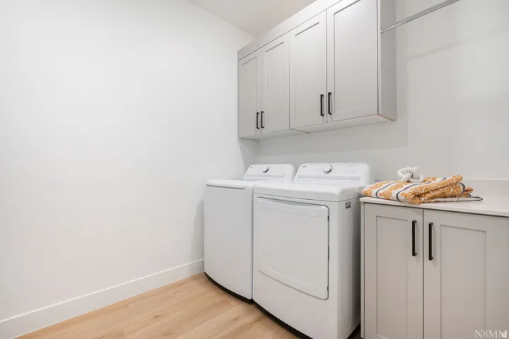 Laundry area featuring light wood-finish flooring, white walls, and built-in shaker-style cabinetry with matte black hardware