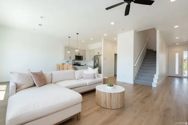 Open-concept living area featuring a generous L-shaped sectional sofa, wood-finish flooring throughout, and recessed ceiling lighting