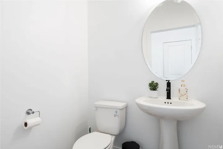 Elegant powder room featuring a pedestal sink with integrated countertop, oval mirror with polished frame, and crisp white tile walls