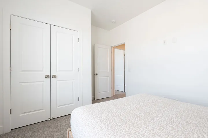 Bright bedroom featuring dual white six-panel closet doors with polished hardware, neutral carpeting, and clean white walls