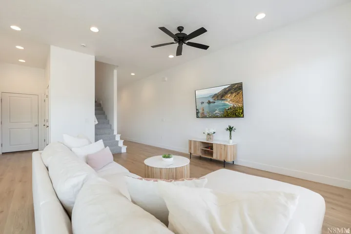 Open-concept living area featuring a curved white sectional sofa, wood-finish flooring throughout, and recessed ceiling lighting