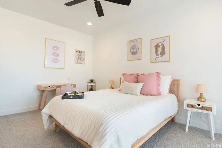 Serene primary bedroom showcasing a natural wood-frame bed with white linens and coordinating pink accent pillows, complemented by matching natural wood nightstands with integrated storage