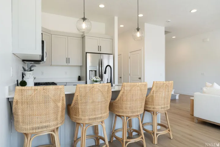 Modern kitchen and dining area featuring white cabinetry with integrated stainless steel appliances, white subway tile backsplash, and a waterfall-edge island