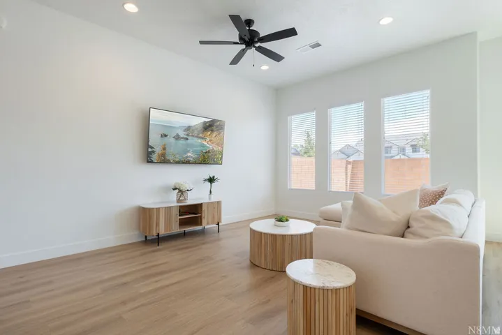 Bright and airy living space showcasing wood-finish flooring, recessed ceiling lighting, and a ceiling fan
