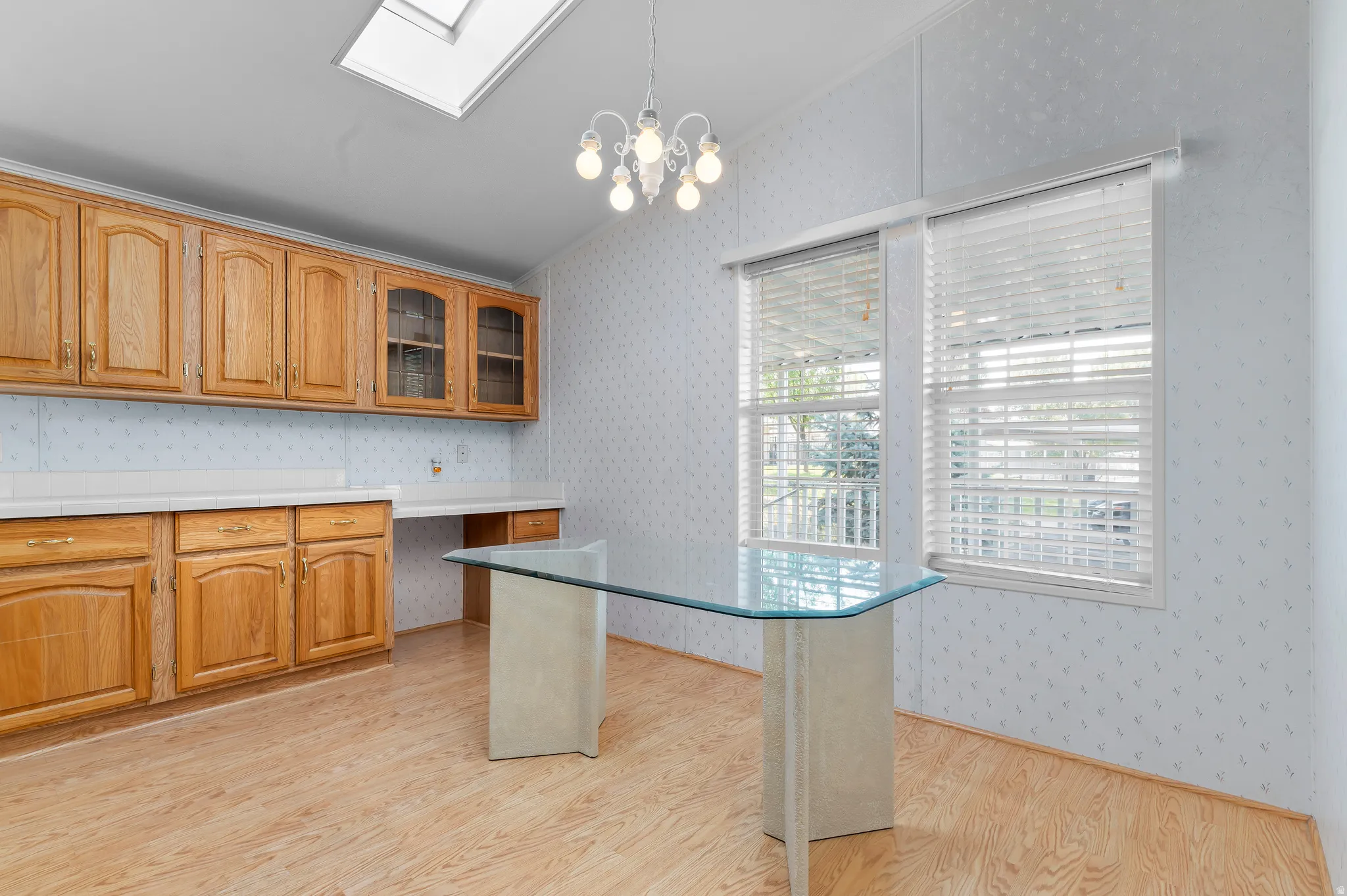 Bright kitchen featuring wood-finish cabinetry with glass-front upper cabinets, wood-finish flooring throughout, and a large island.