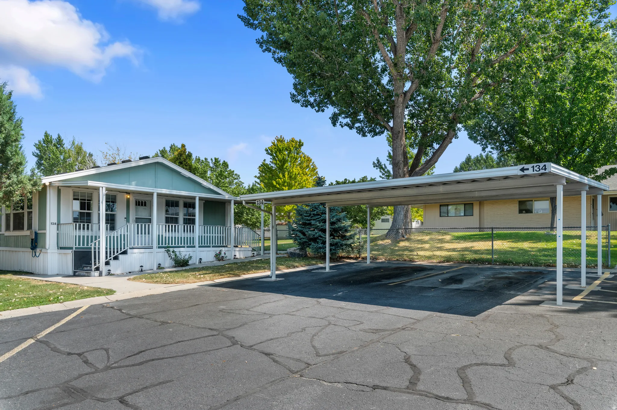 Exterior residence featuring a covered front porch with white railings, a light green facade, and a dedicated two-car carport