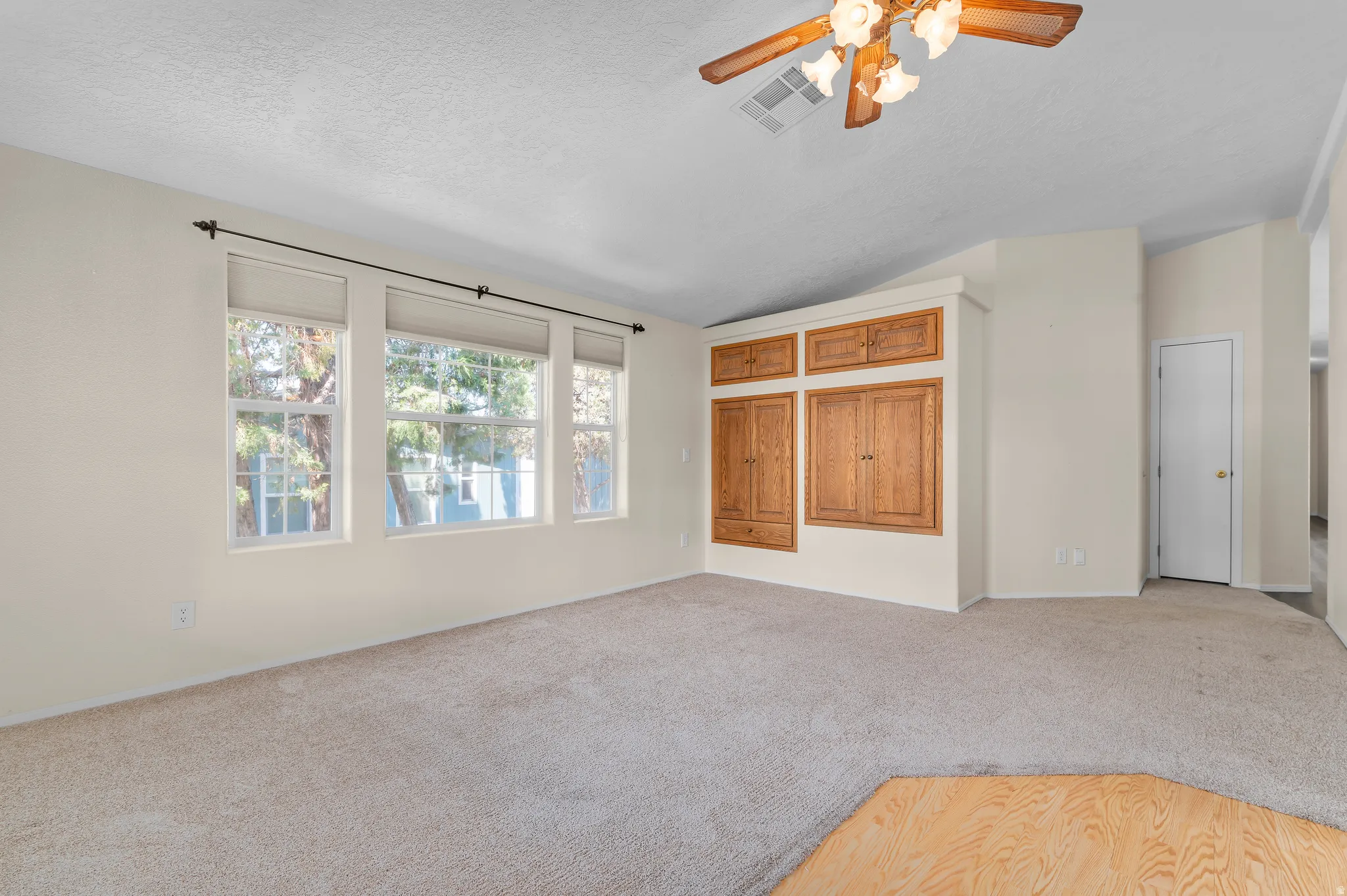 Featuring multiple windows, built-in wooden cabinetry, a ceiling fan with integrated lighting, and neutral carpet flooring.