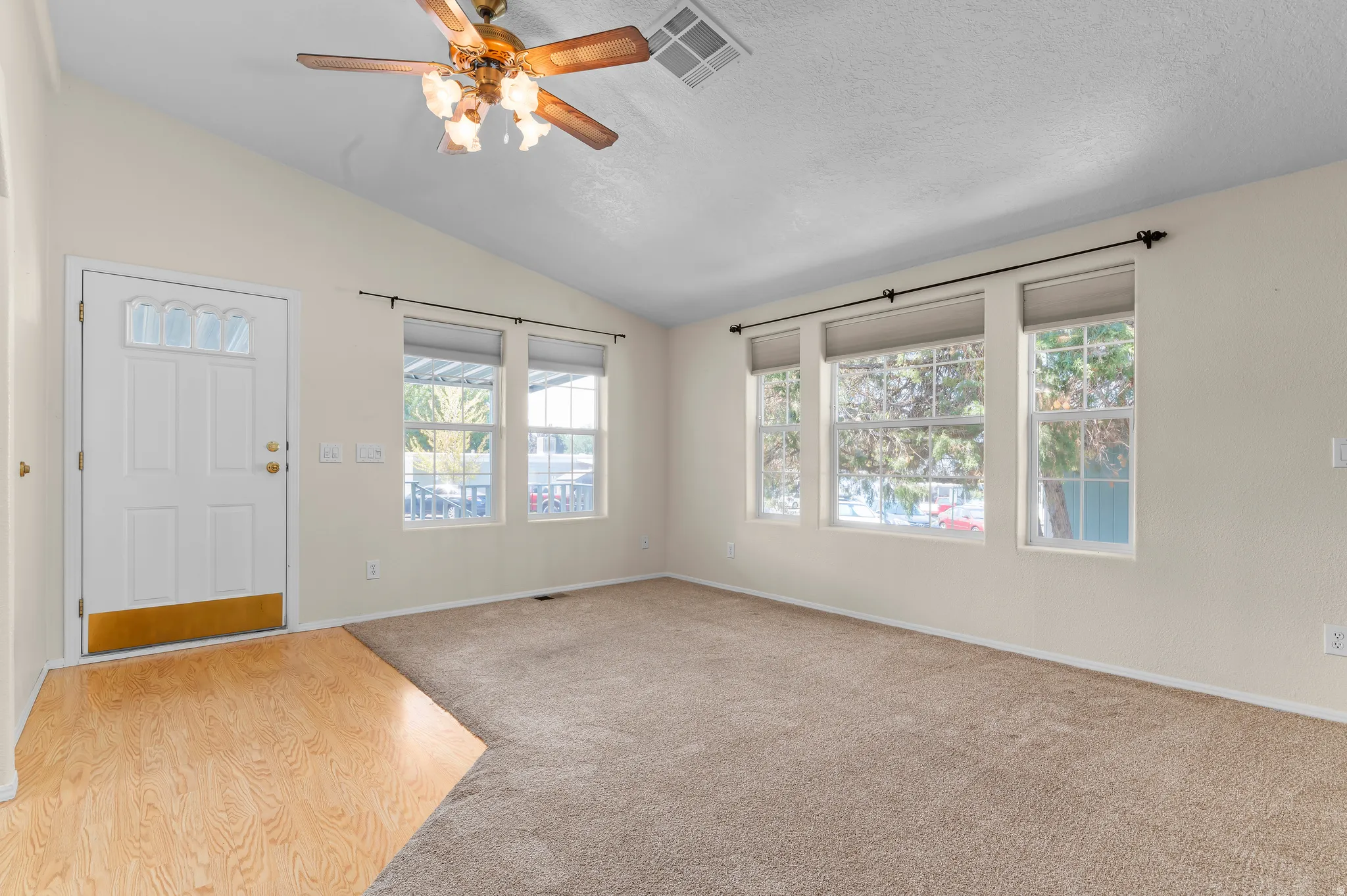 Vaulted ceilings define this open space, featuring a paneled entry door with decorative glass, wood-finish flooring, and multiple windows.