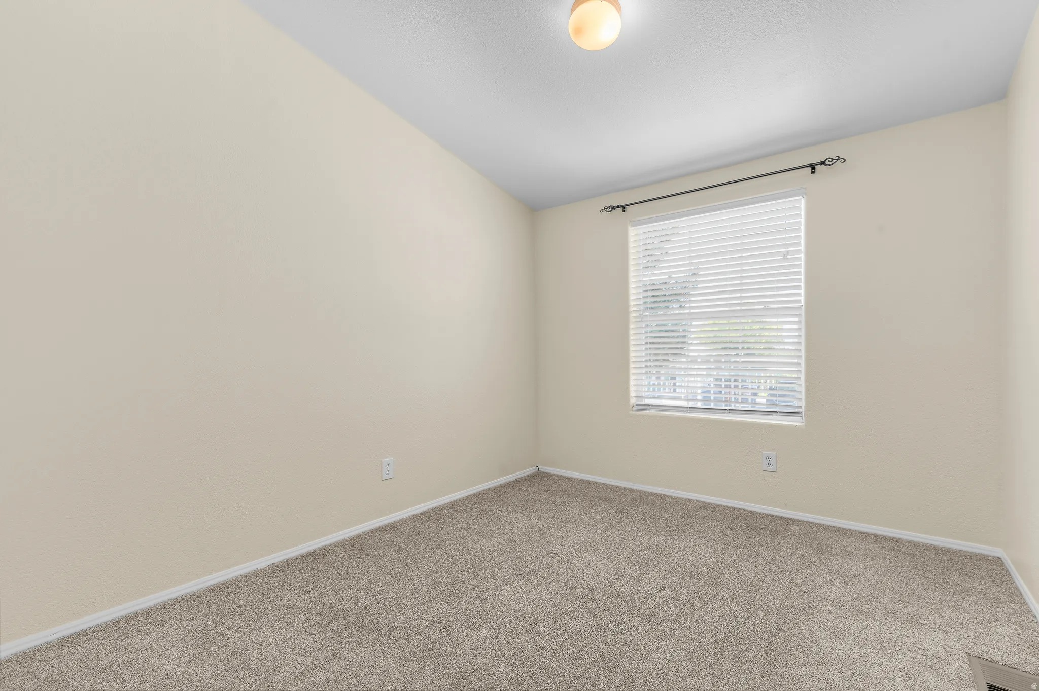 Neutral tone walls and carpeting throughout a room featuring a window with white blinds.