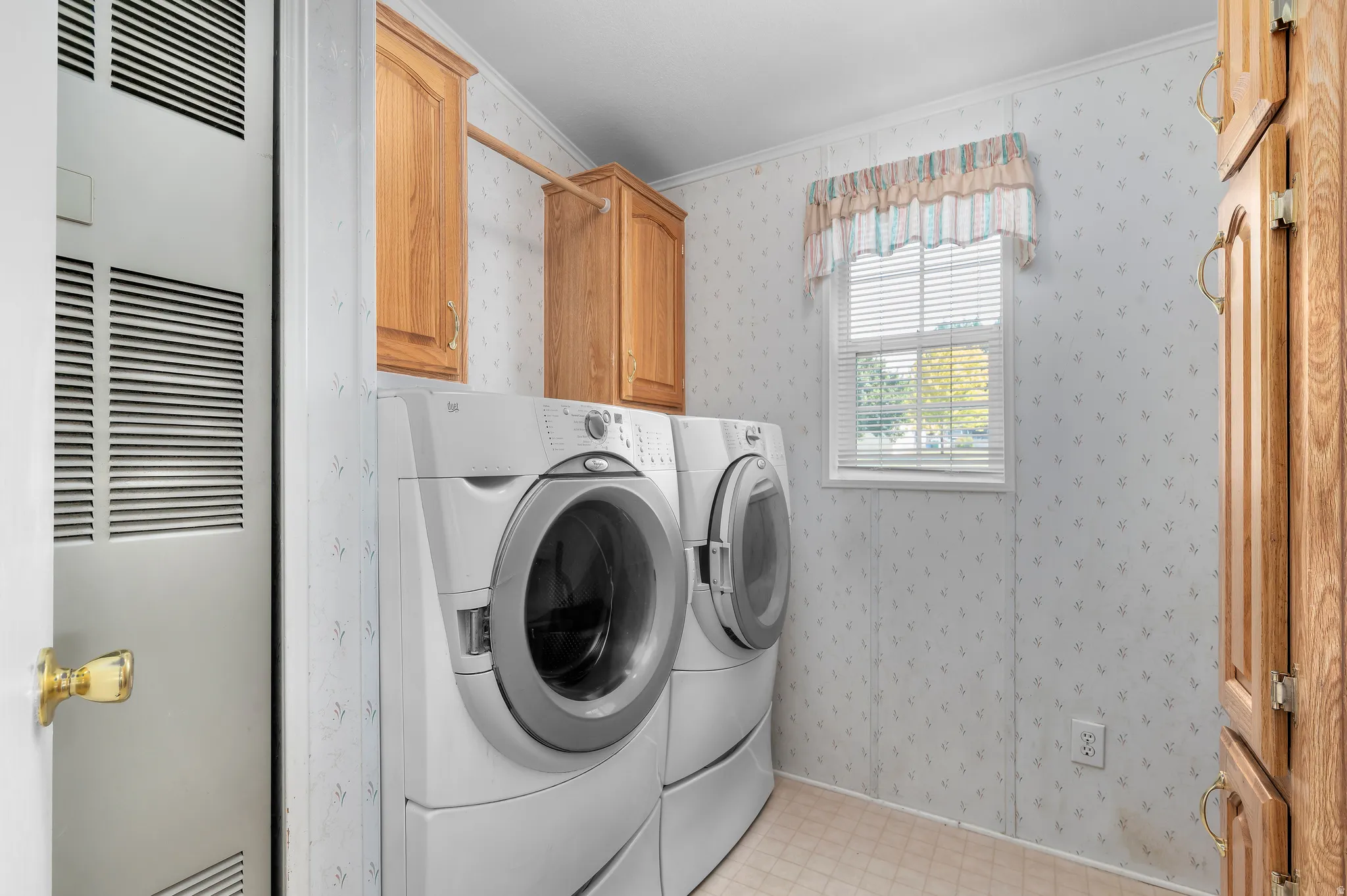 Utility room featuring wood-finish cabinetry, a single window with blinds, and vinyl flooring.