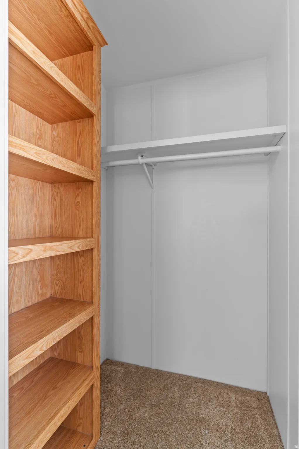 Built-in light wood-tone shelving with crown molding, white walls, and neutral carpet flooring