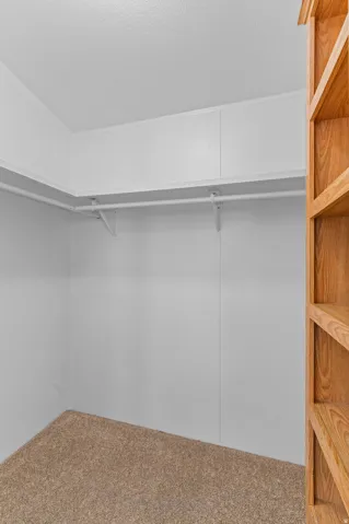 Spacious walk-in closet featuring white drywall construction, polished concrete flooring, and a sturdy metal hanging rod system for optimal storage and organization