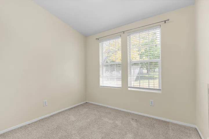 Room featuring two windows with horizontal blinds, neutral-toned walls, and wall-to-wall carpeting