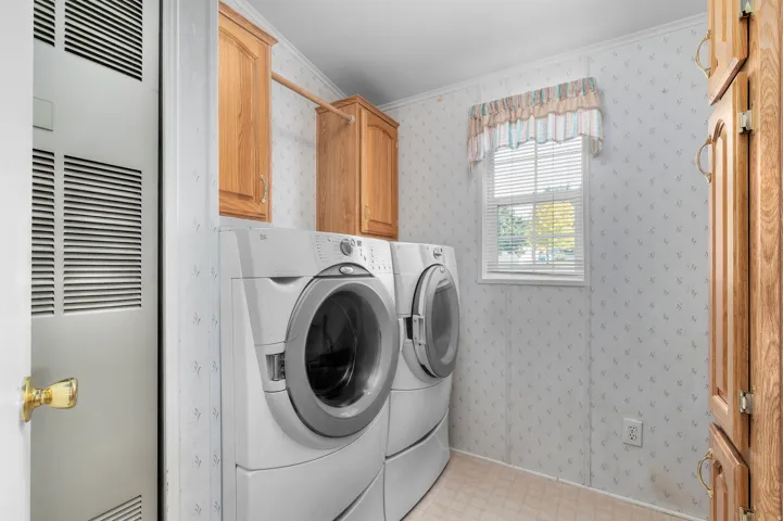 Utility room featuring wood-finish cabinetry, a single window with blinds, and vinyl flooring.