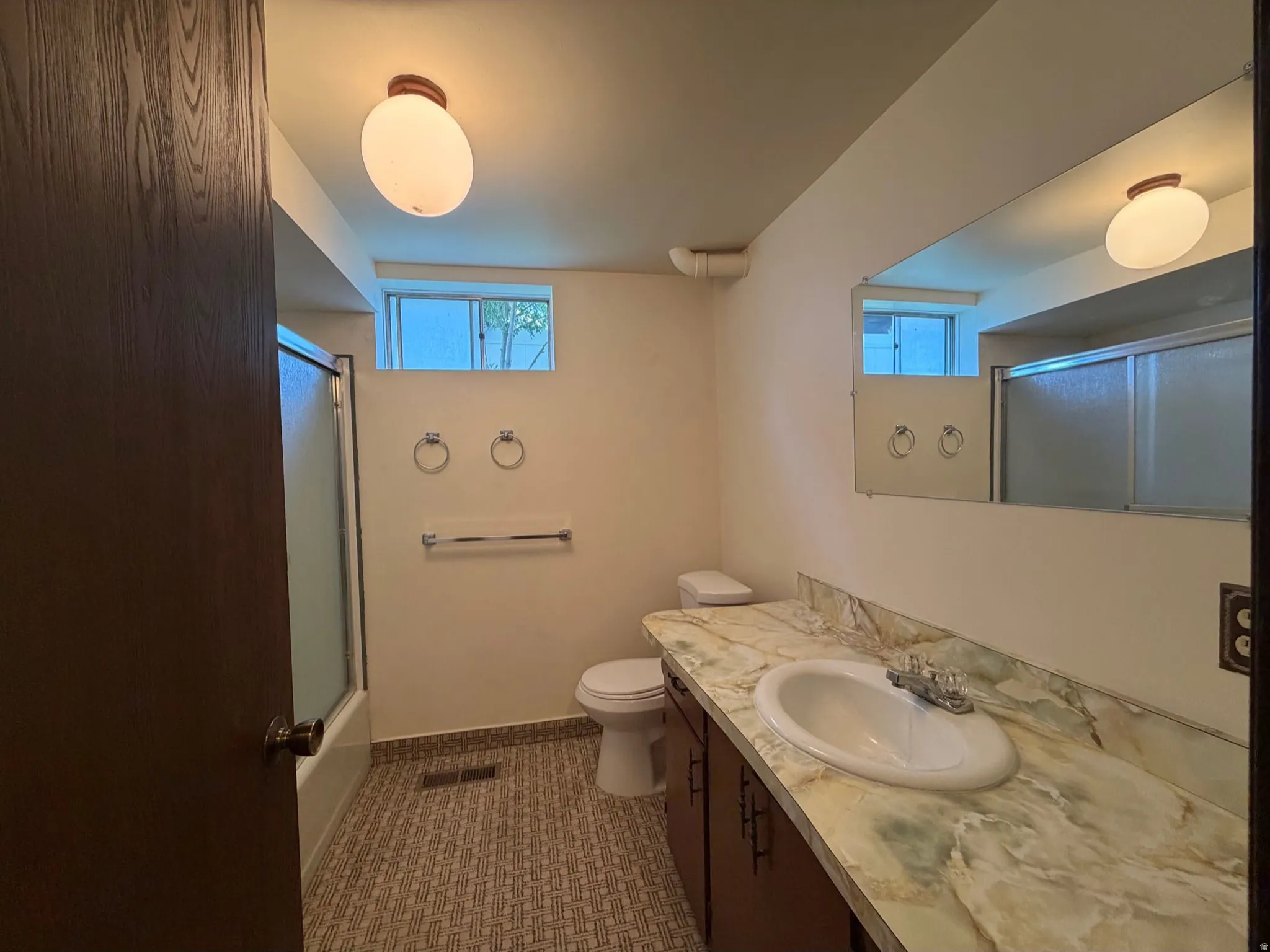 Bright bathroom featuring recessed and wall-mounted lighting, dual windows with natural light, wood-finish flooring, patterned tile accent wall, and white ceramic fixtures including pedestal sink and bathtub with surround