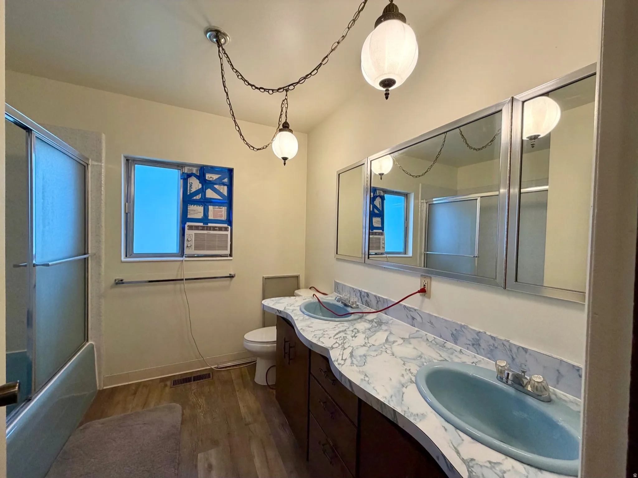 Bathroom featuring a double vanity with blue basins and a patterned countertop, a toilet, a window, and a shower enclosure