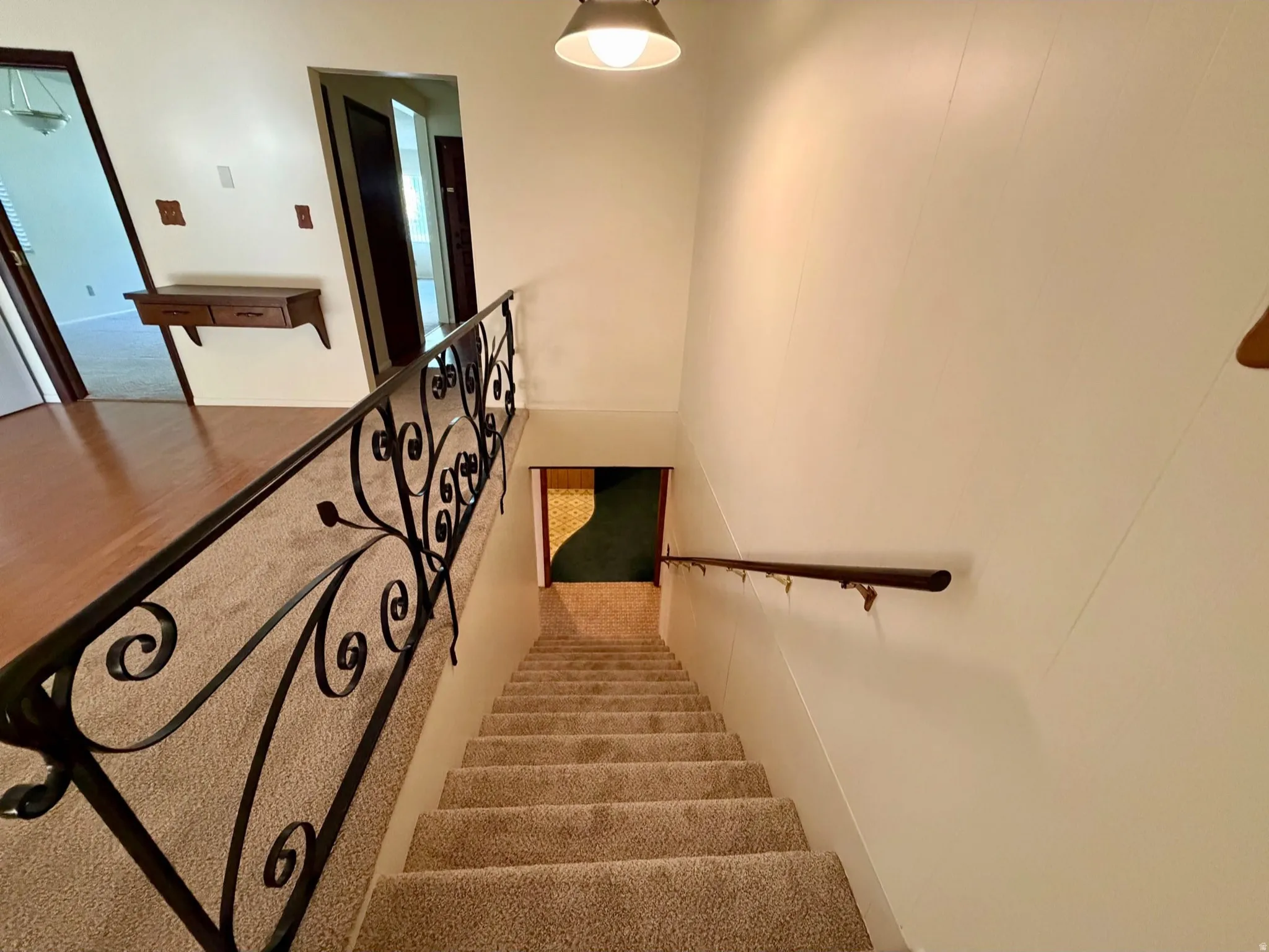 Wrought iron railing with decorative scrollwork, wall-mounted sconce lighting, wood-finish wall paneling, and carpeted stairs