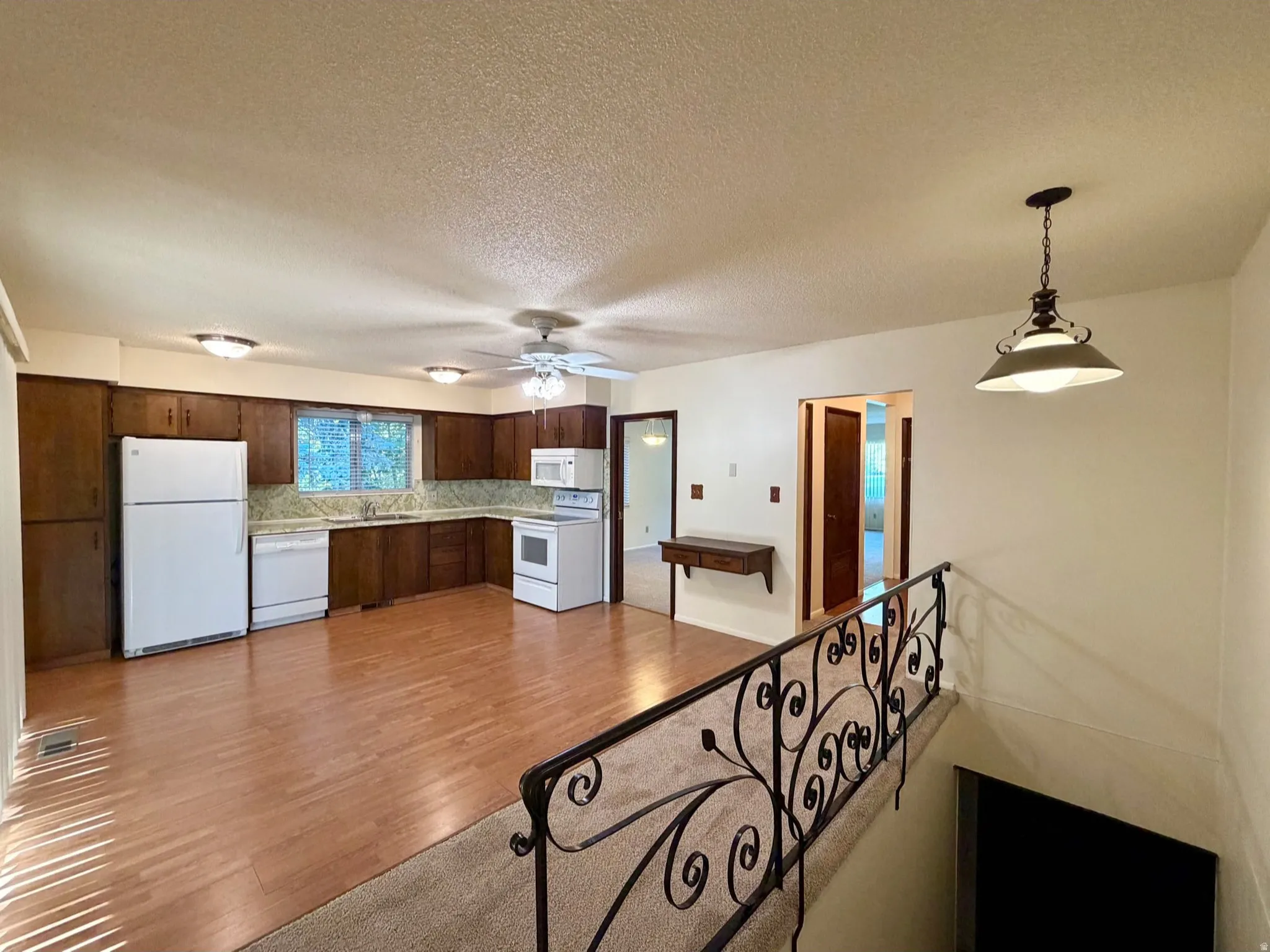 Open-concept living space featuring wood-finish flooring, a kitchen with rich wood cabinetry, and a ceiling fan