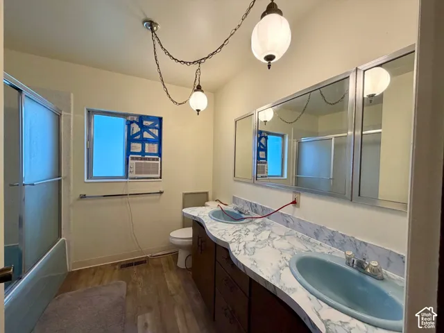 Bathroom featuring a double vanity with blue basins and a patterned countertop, a toilet, a window, and a shower enclosure