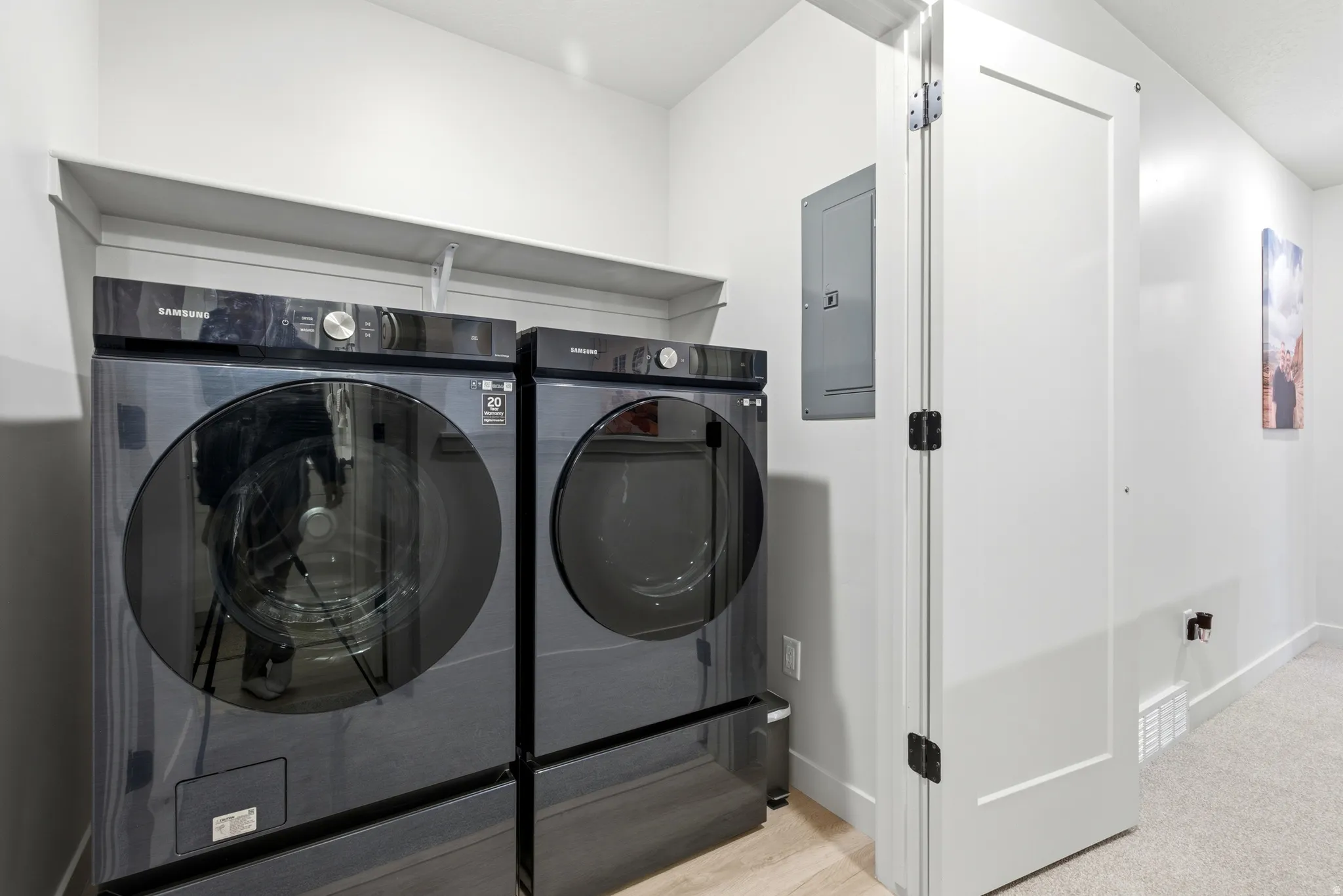 Dedicated laundry area featuring a washer and dryer, an overhead shelf, light wood-finish flooring, and a white interior door with black hardware