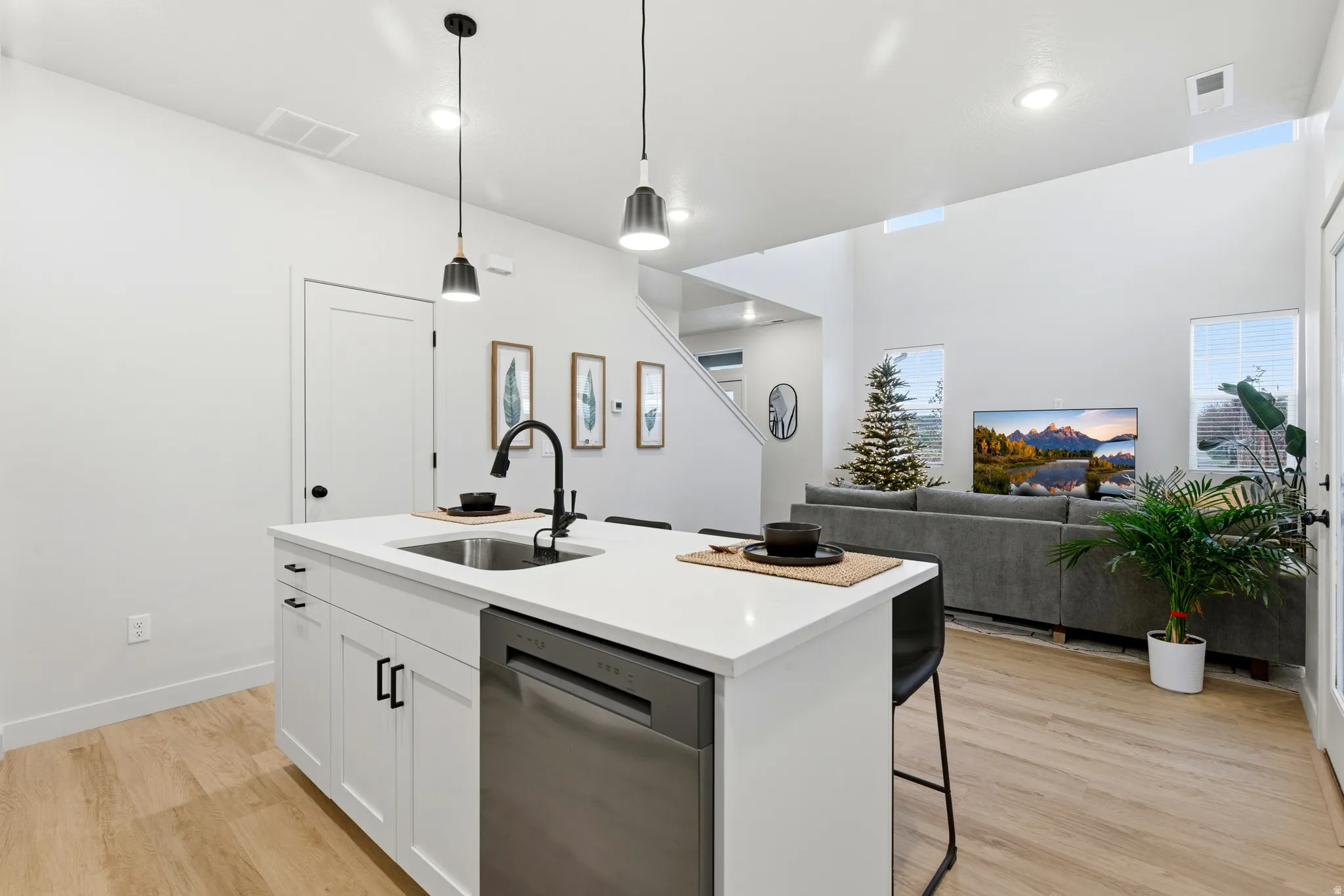 Kitchen island featuring white cabinetry, a stainless steel dishwasher, a single-basin sink with a matte black faucet, and pendant lighting