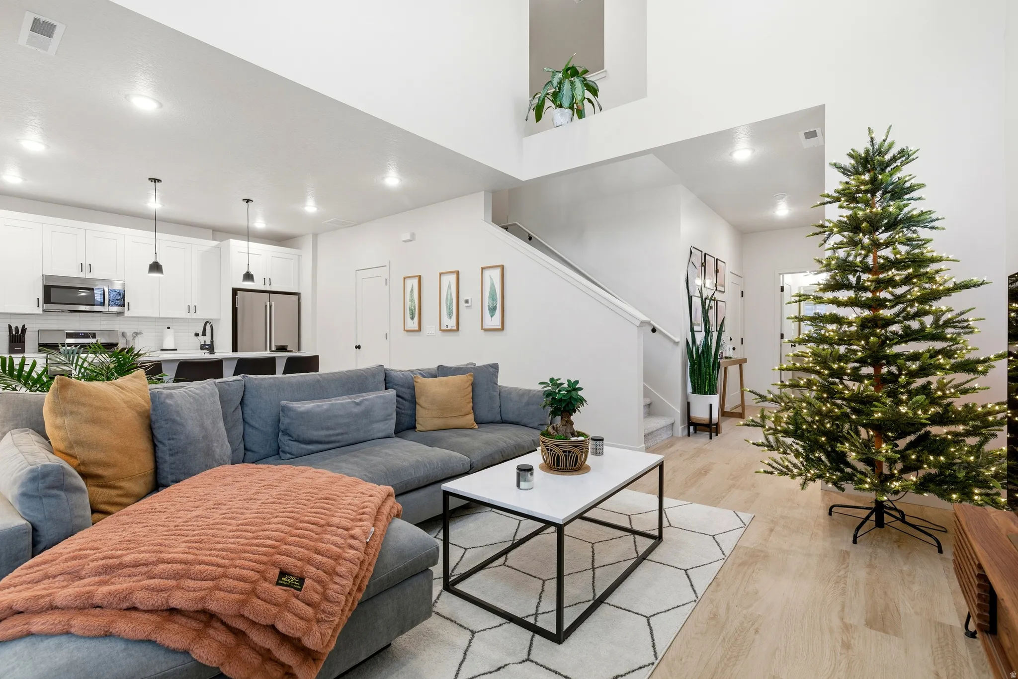 Open-concept living area featuring high ceilings, wood-finish flooring, a contemporary kitchen with white cabinetry, stainless steel appliances, and a breakfast bar