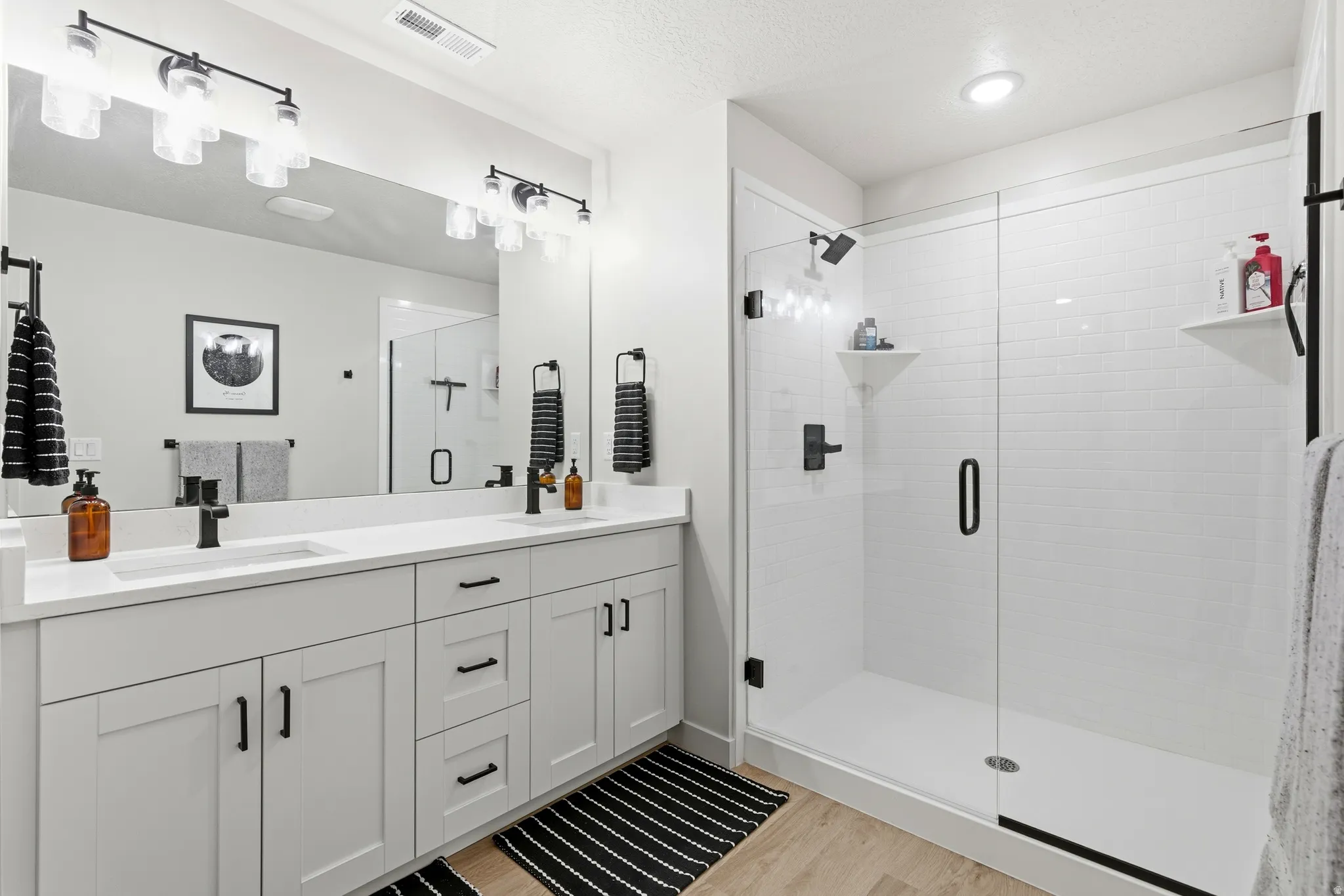 Modern bathroom featuring a dual vanity with white shaker-style cabinetry, quartz countertops, and matte black hardware