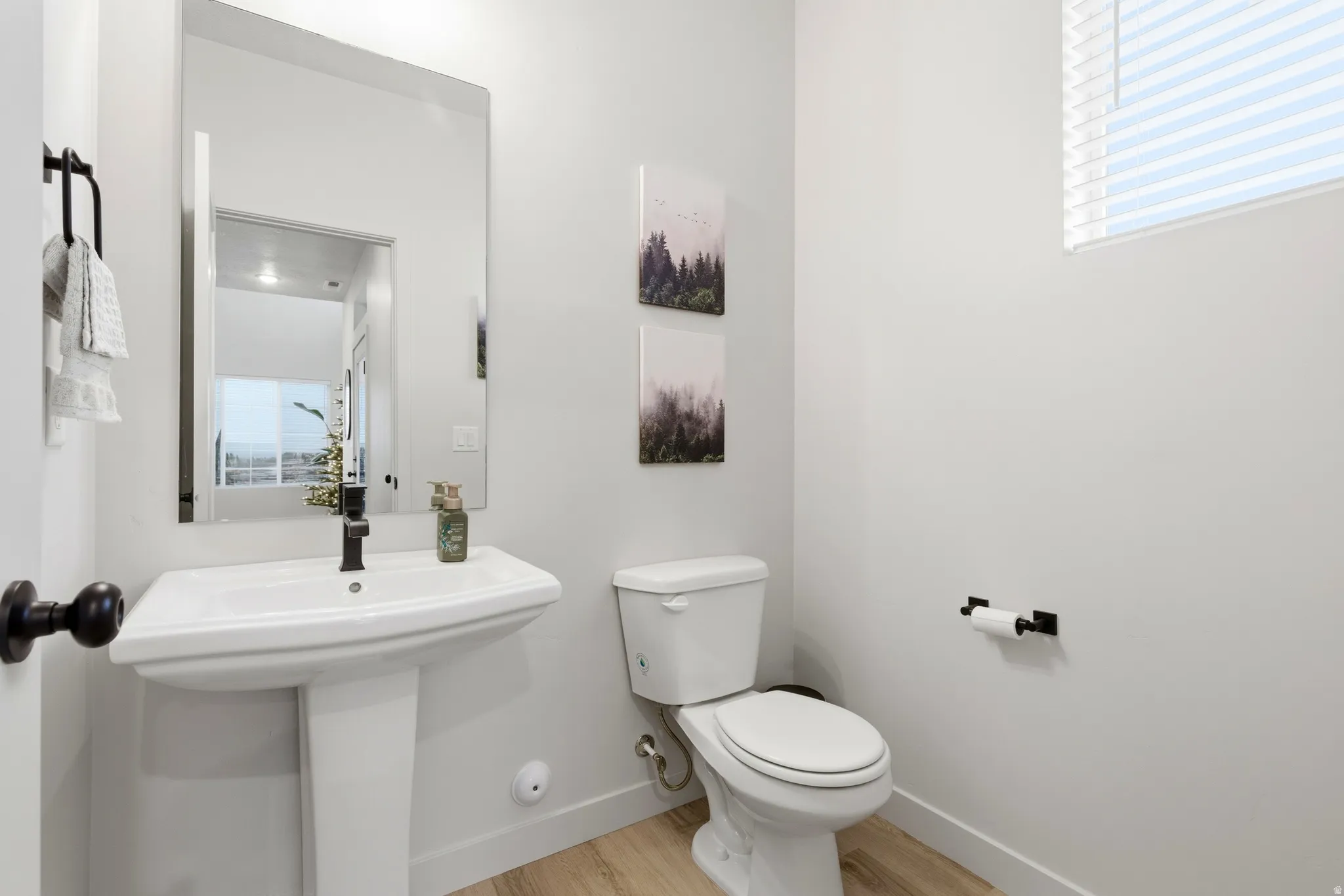Modern powder room featuring a white pedestal sink with a matte black faucet, a contemporary toilet, and light wood-finish flooring