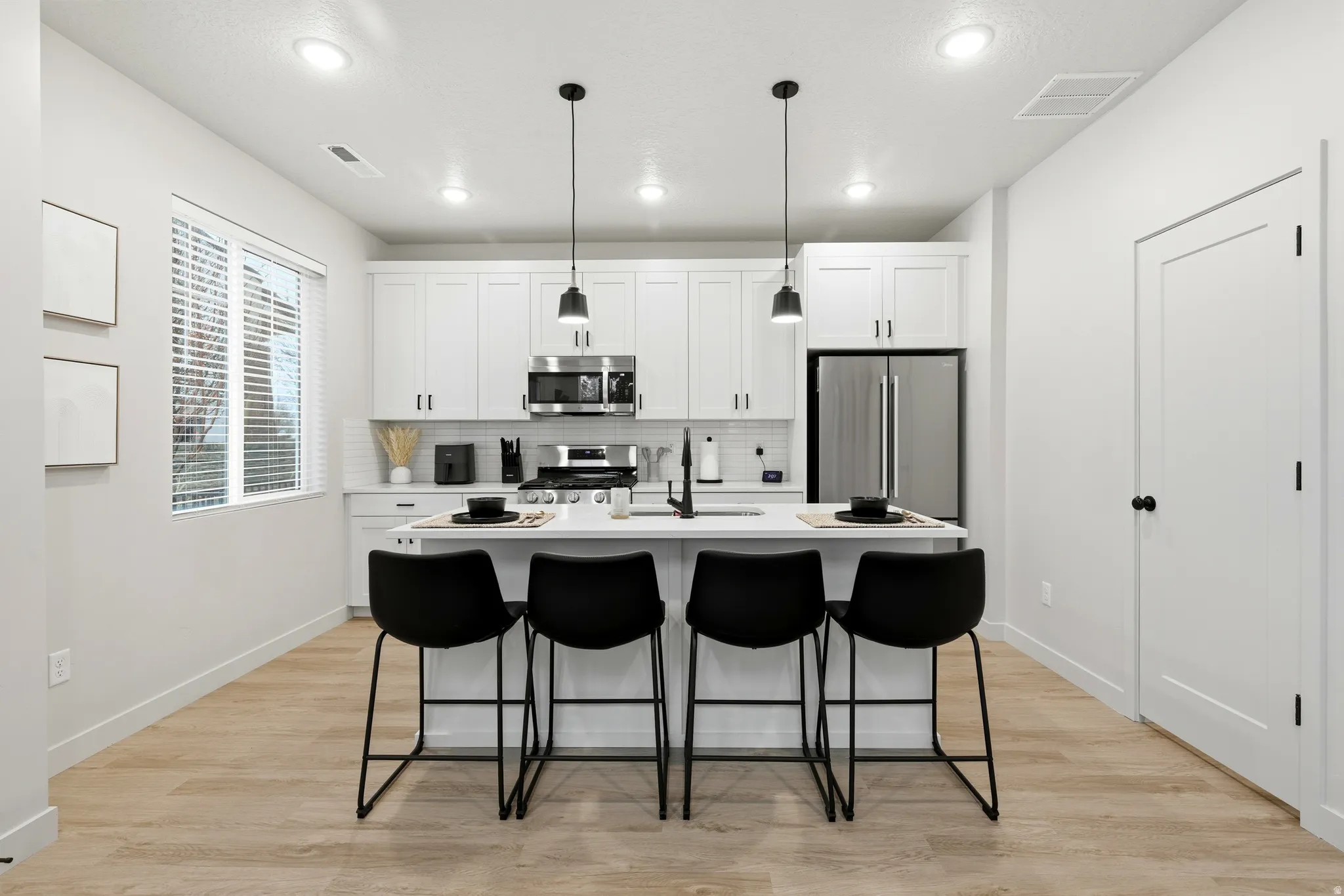 Contemporary kitchen featuring white cabinetry, stainless steel appliances, a white subway tile backsplash, and light wood-finish flooring