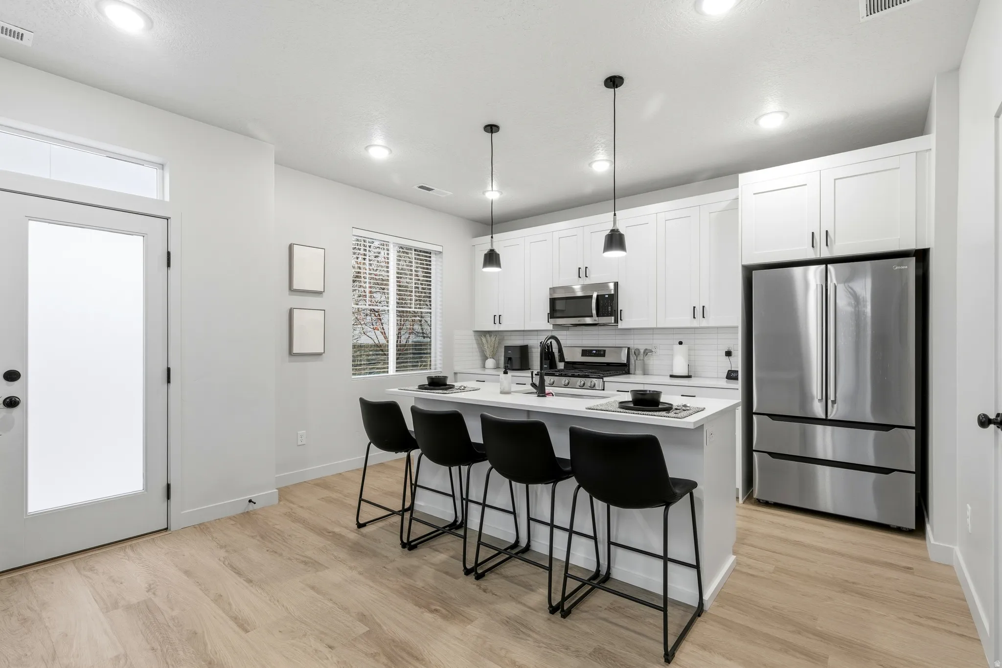 Kitchen featuring an island with pendant lighting, stainless steel appliances, white cabinetry, a subway tile backsplash, and wood-finish flooring