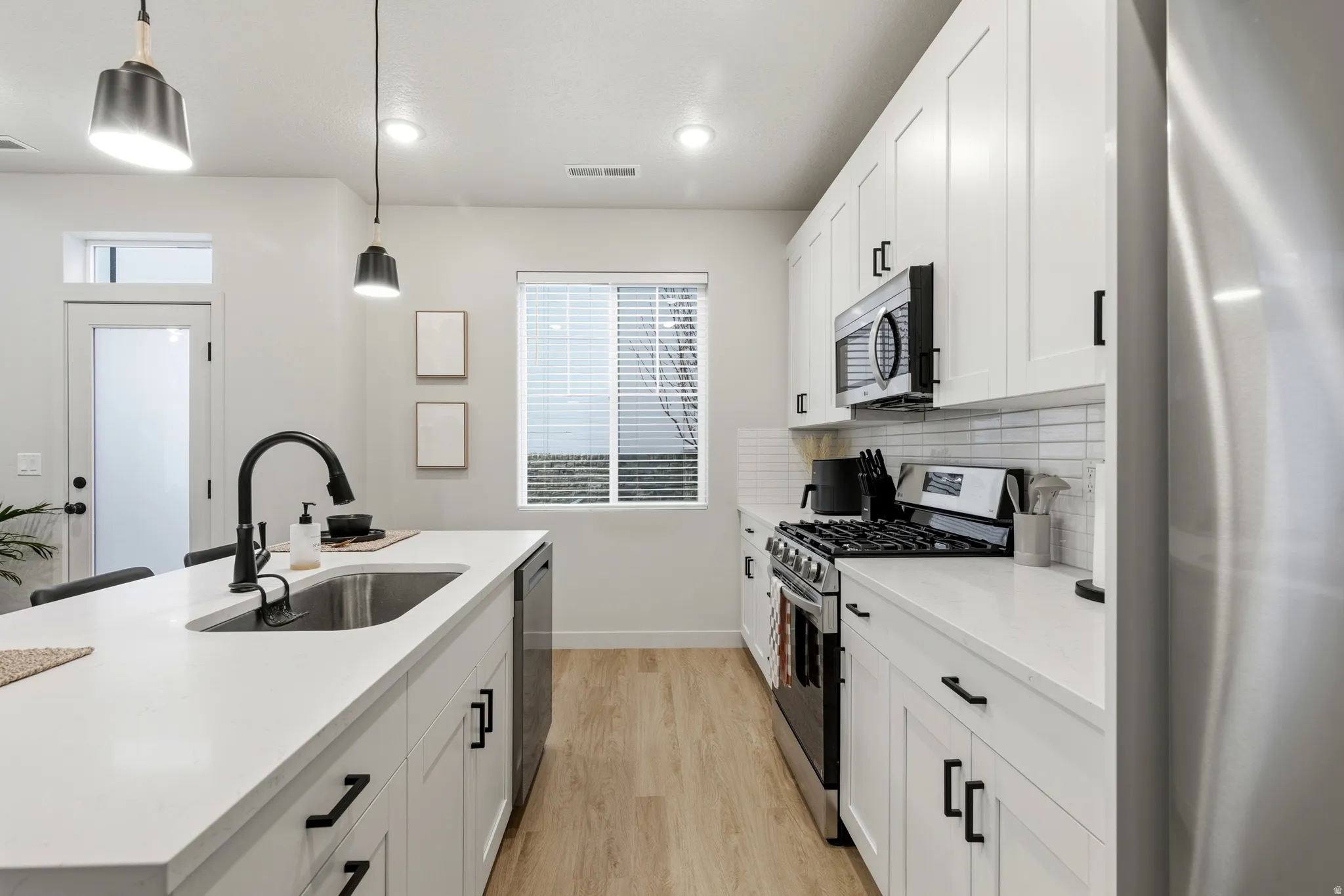 Modern kitchen featuring white shaker cabinetry, stainless steel appliances, a center island with undermount sink, and wood-finish flooring
