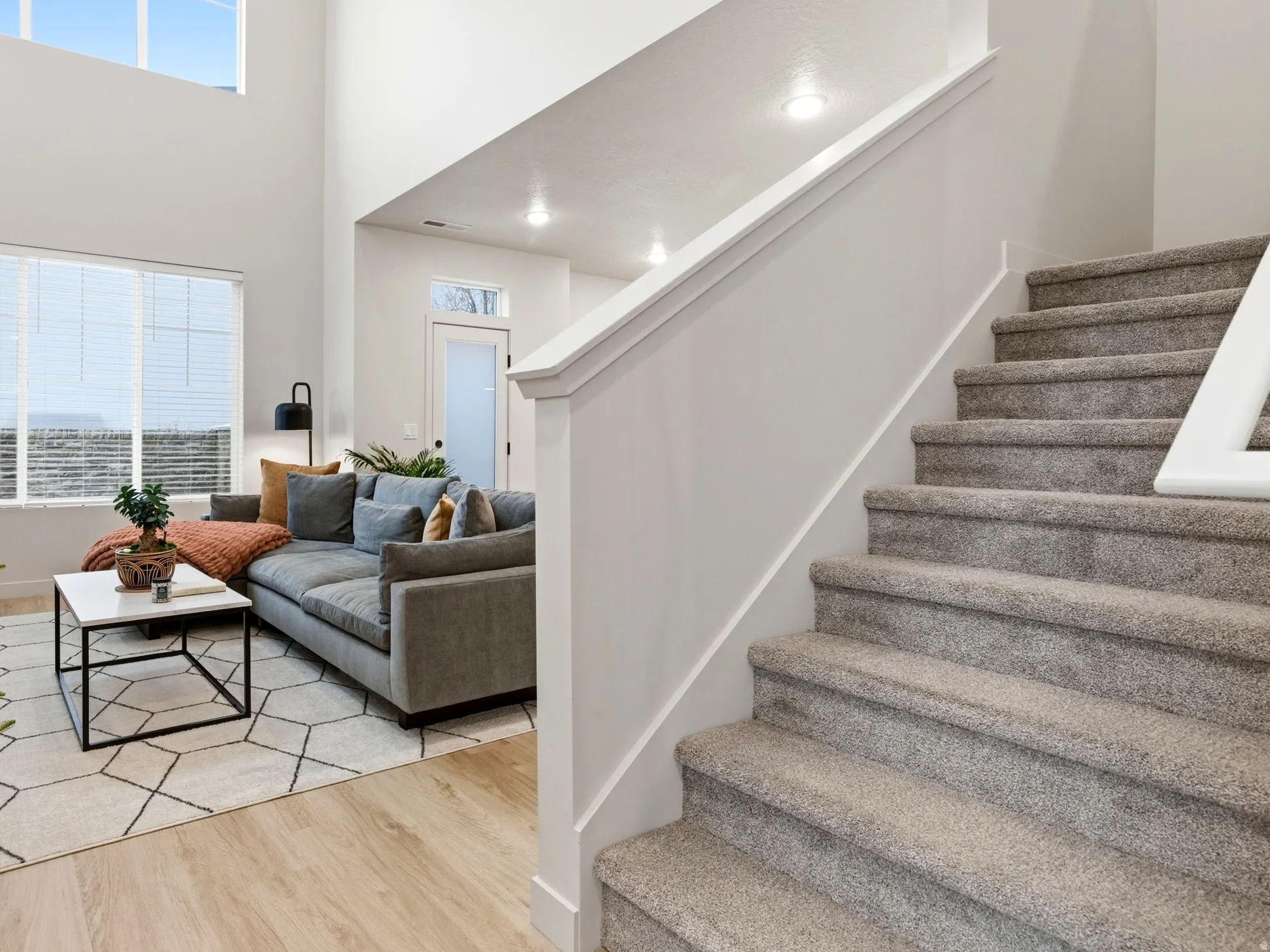 Two-story foyer featuring a carpeted staircase with white railing, recessed lighting, and light wood-finish flooring
