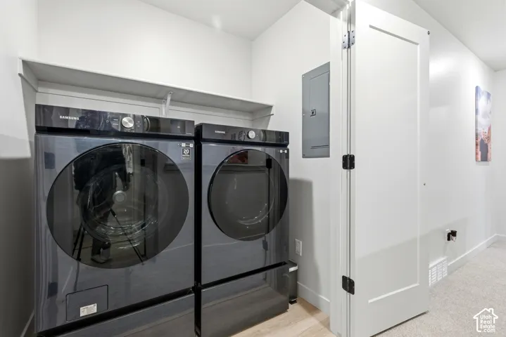 Dedicated laundry area featuring a washer and dryer, an overhead shelf, light wood-finish flooring, and a white interior door with black hardware