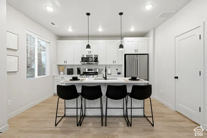 Contemporary kitchen featuring white cabinetry, stainless steel appliances, a white subway tile backsplash, and light wood-finish flooring