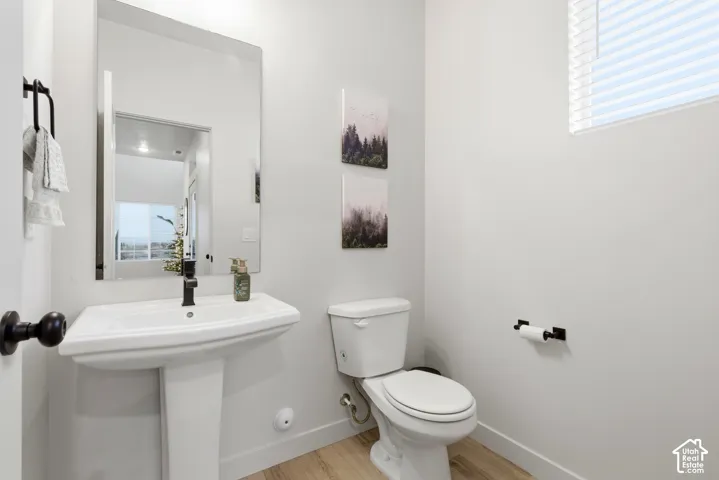 Modern powder room featuring a white pedestal sink with a matte black faucet, a contemporary toilet, and light wood-finish flooring