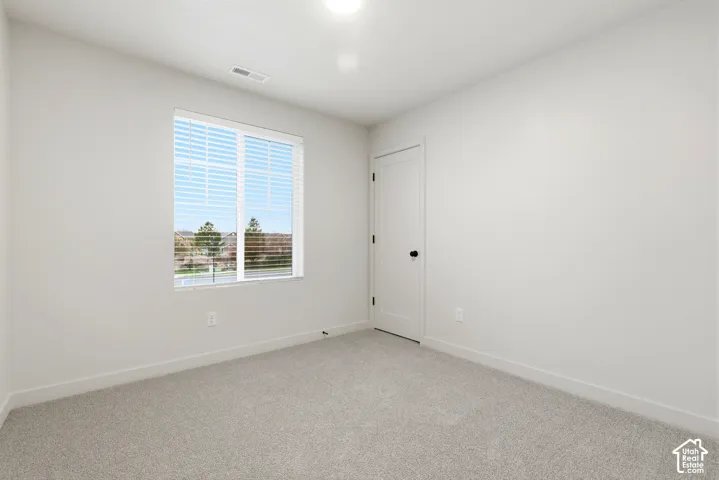 Neutral-toned room featuring a single window with blinds, light gray wall-to-wall carpeting, white walls, and a white interior door with black hardware
