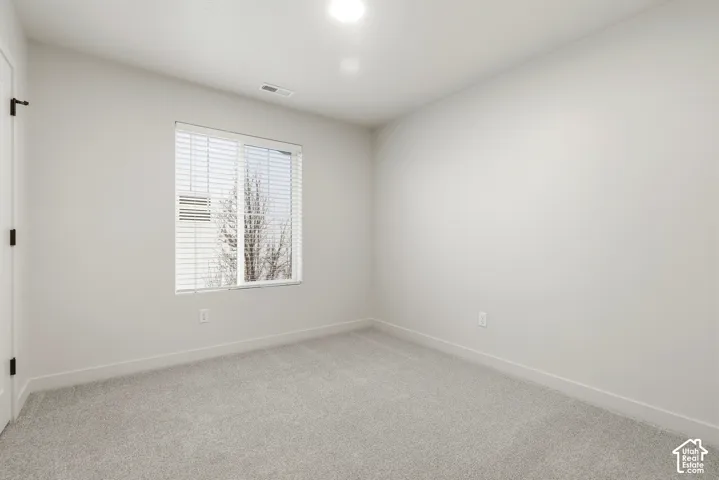 Neutral-toned room featuring a window with blinds, light gray carpet, and white baseboards