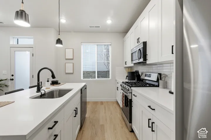 Modern kitchen featuring white shaker cabinetry, stainless steel appliances, a center island with undermount sink, and wood-finish flooring
