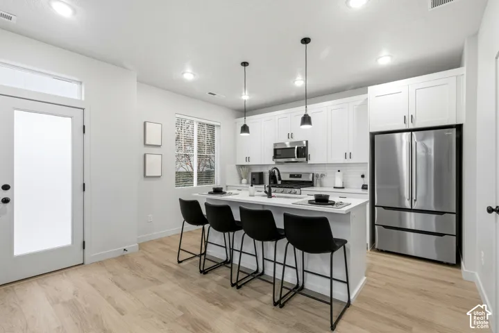 Kitchen featuring an island with pendant lighting, stainless steel appliances, white cabinetry, a subway tile backsplash, and wood-finish flooring